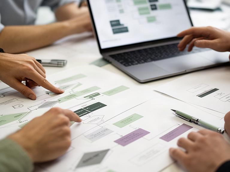 Close view of a team planning smart contract workflows beside a laptop and printed blockchain diagrams